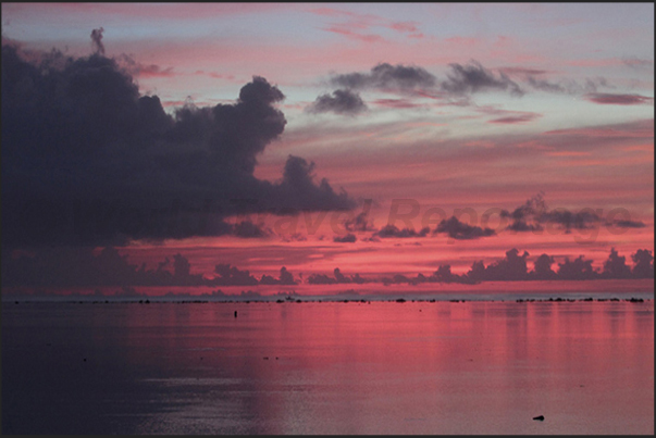 Sunset over the Pacific Ocean while the red sky is reflected on the calm waters of the lagoon