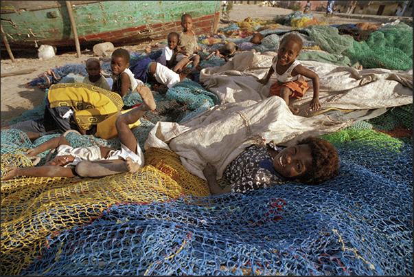 A group of children play on the beach, on a pile of fishing nets
